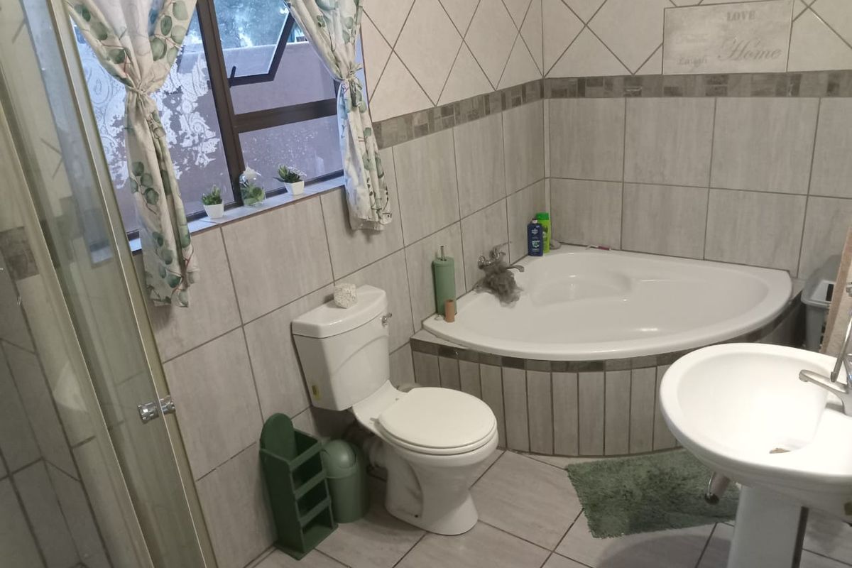 A functional bathroom featuring a corner bathtub, pedestal basin, and a separate shower enclosure with neutral wall and floor tiling.