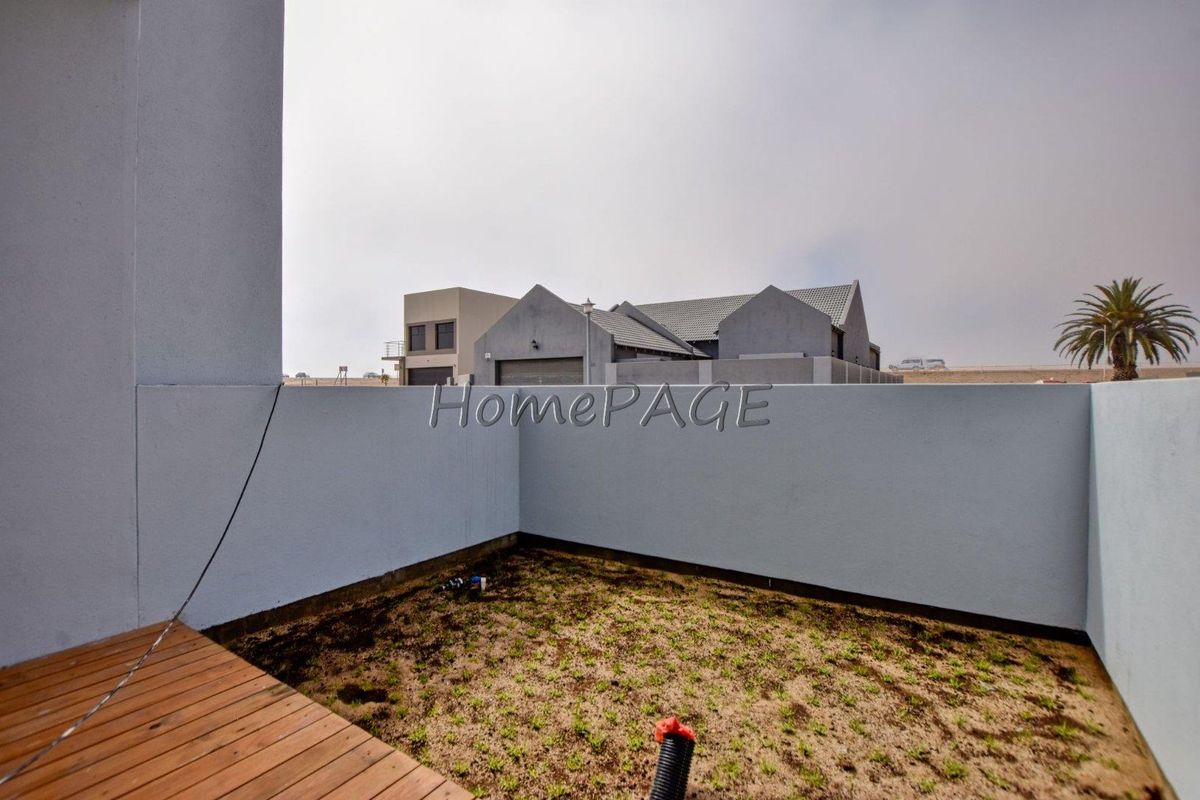 A rear outdoor area featuring timber decking and a boundary wall, currently with sparse ground cover and exposed utility infrastructure.