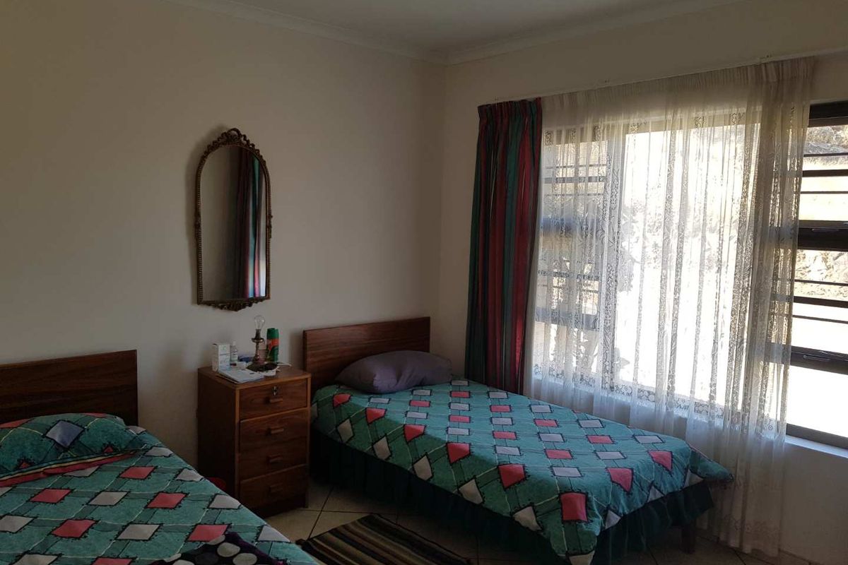 A bedroom featuring tiled flooring and a large window with security bars, providing natural light.