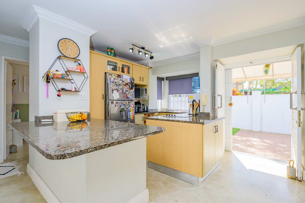 Functional kitchen featuring granite countertops, light wood cabinetry, and a central island, with direct access to an outdoor patio area.