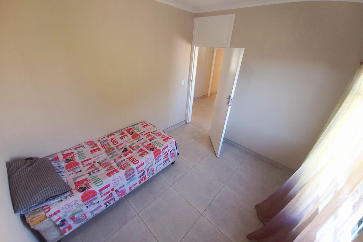 A simple bedroom featuring neutral wall paint and tiled flooring, with a doorway leading to an adjacent hallway.