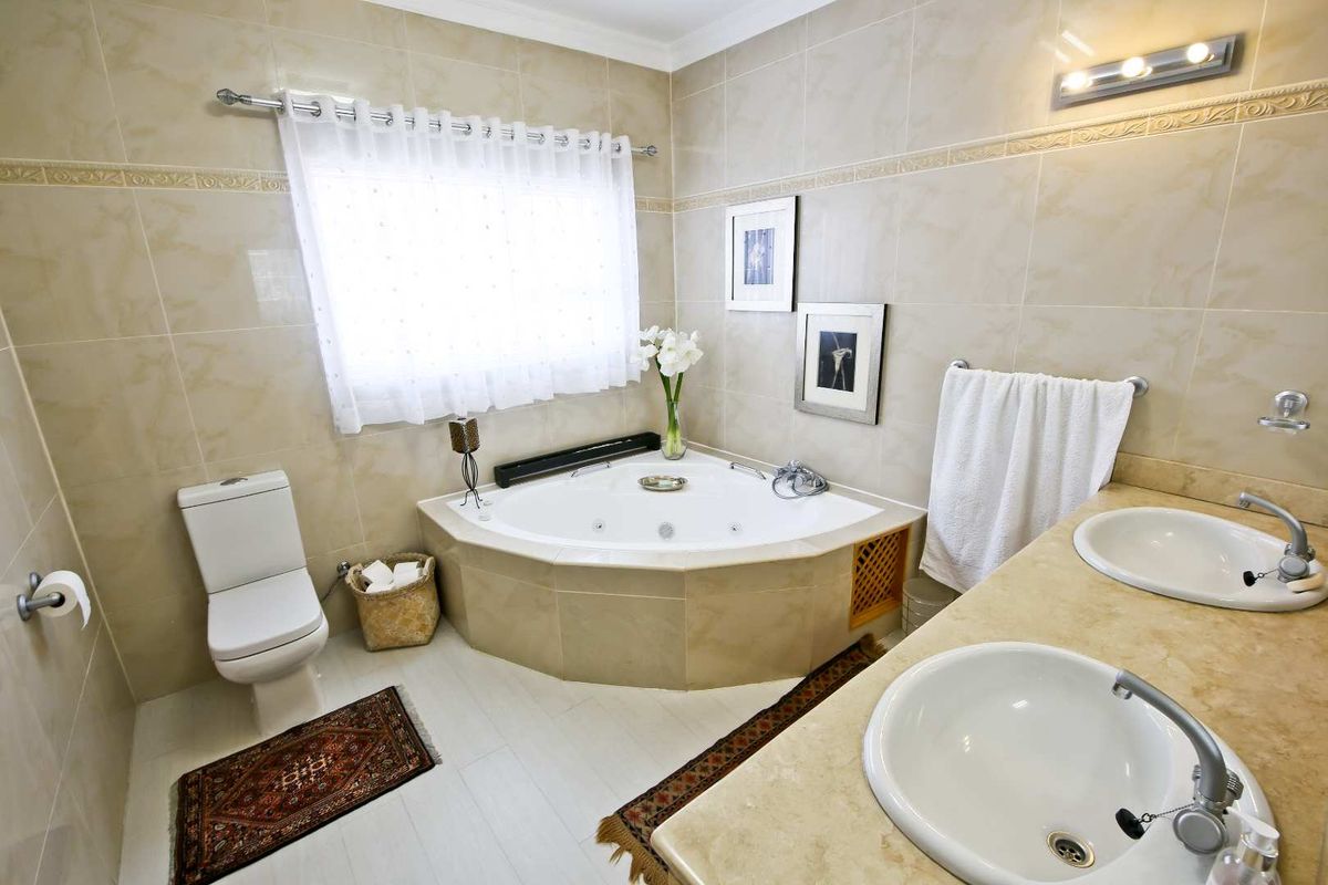 A spacious bathroom featuring a corner jetted tub, dual vanity sinks with stone countertops, and neutral wall tiling.