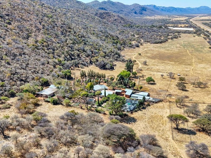 Aerial view of a rural small holding property featuring multiple structures, a swimming pool, and surrounding natural landscape.