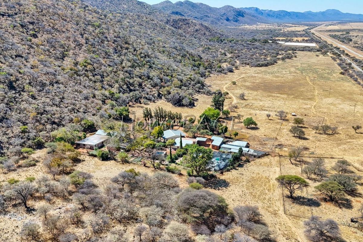 Aerial view of a rural small holding property featuring multiple structures, a swimming pool, and surrounding natural landscape.