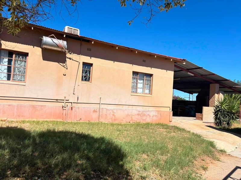Rear exterior view of the house featuring a covered patio area, solar geyser, and air conditioning unit, showing signs of weathered exterior finishes.