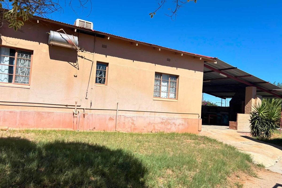Rear exterior view of the house featuring a covered patio area, solar geyser, and air conditioning unit, showing signs of weathered exterior finishes.