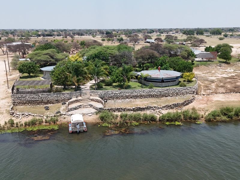 Aerial view of a riverfront small holding featuring a stone retaining wall, landscaped gardens, and private boat mooring access.