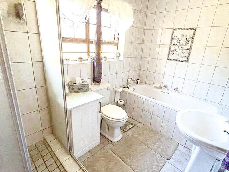 A functional bathroom featuring a shower enclosure, bathtub, pedestal basin, and toilet with neutral wall and floor tiling.