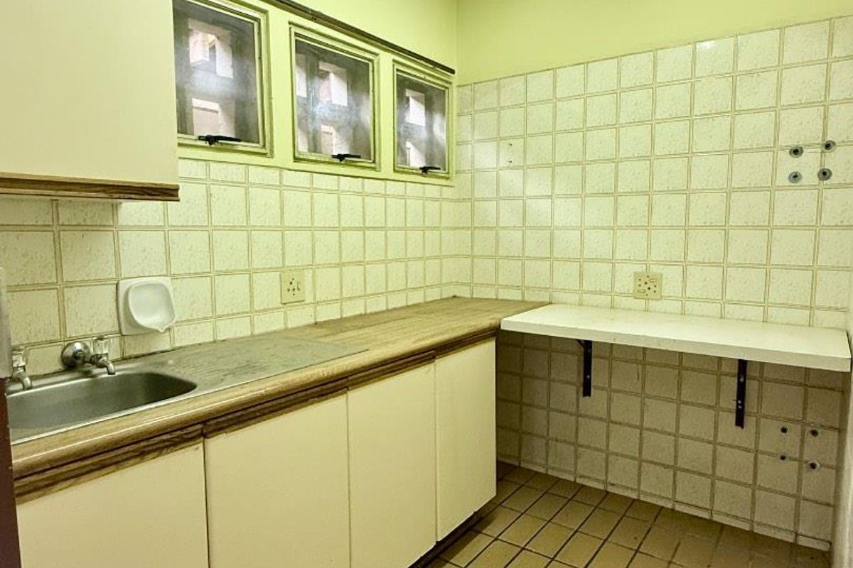 A functional, empty kitchen space featuring built-in cabinetry, a stainless steel sink, tiled backsplash, and tiled flooring, ready for modernization.