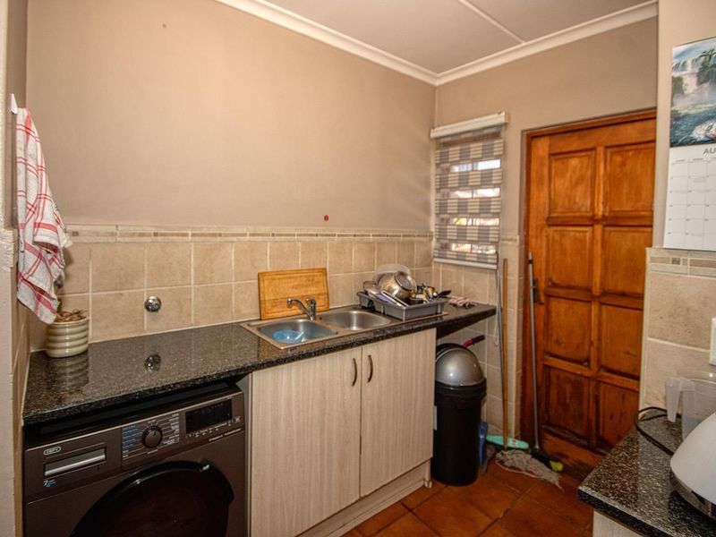 Functional scullery area featuring granite countertops, a double sink, built-in cabinetry, and tiled finishes, providing a practical space for laundry and kitchen prep.