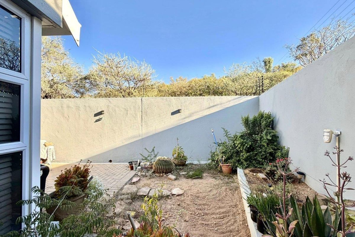 A private rear courtyard featuring a paved patio area, perimeter boundary walls, and established garden beds with potential for landscaping.
