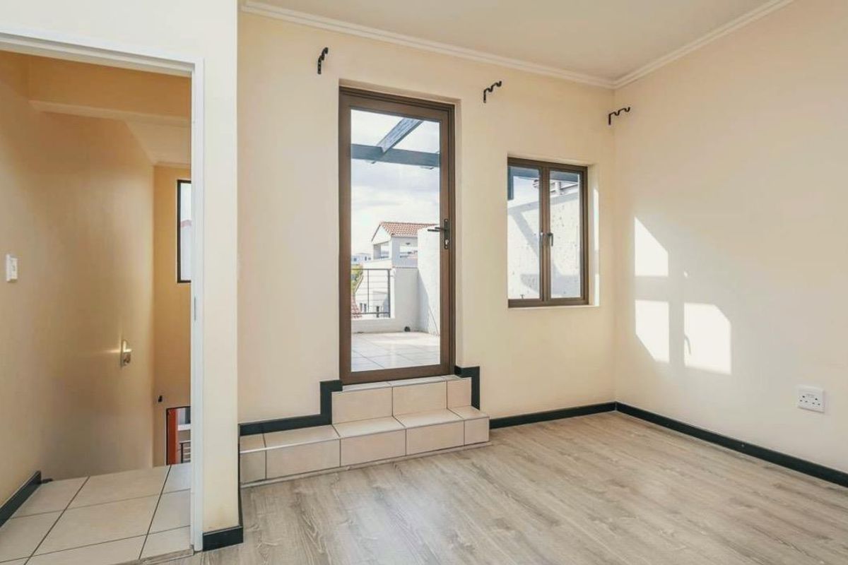 An empty living area featuring light wood-look flooring, a raised tiled threshold leading to a balcony, and neutral wall finishes.
