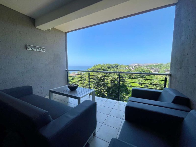 A covered balcony featuring tiled flooring, a metal balustrade, and expansive views of the surrounding greenery and ocean.