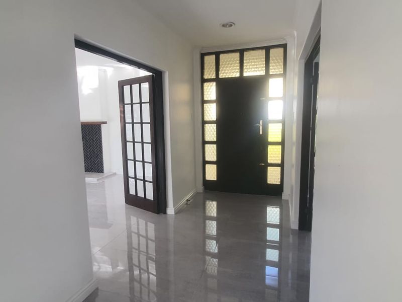 A bright and spacious entrance hall featuring polished tiled flooring, modern recessed lighting, and elegant dark-framed glass panel doors.