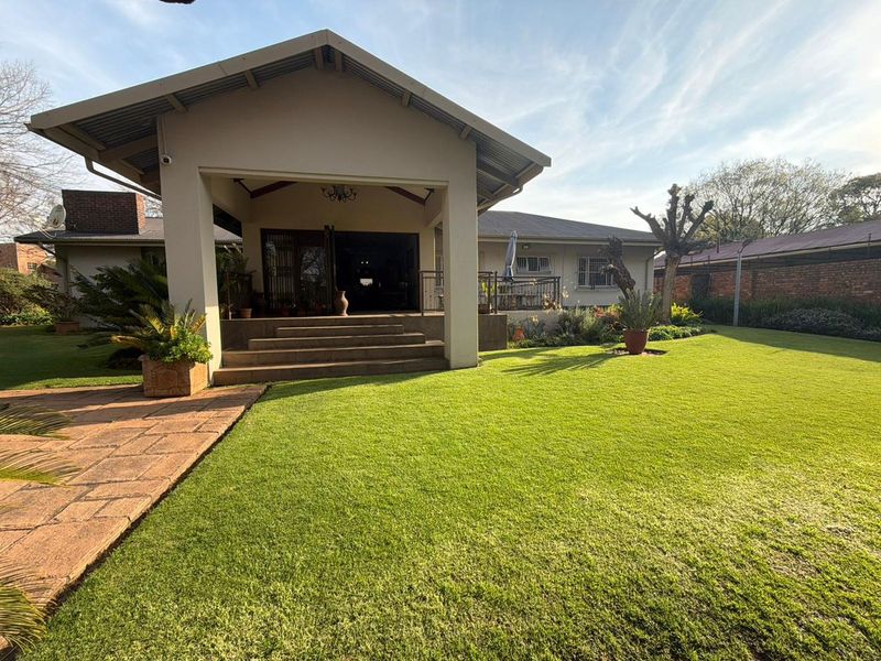 A well-maintained rear exterior view featuring a spacious covered patio, concrete steps, and a large, manicured lawn area.