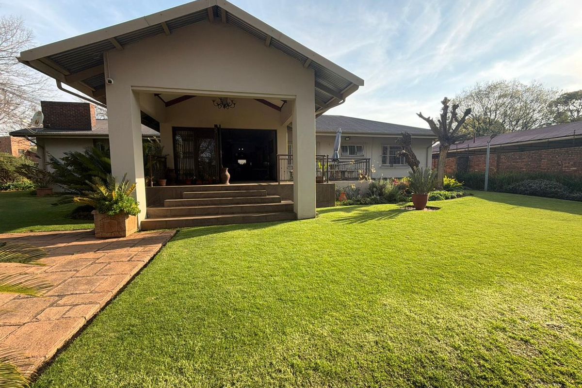 A well-maintained rear exterior view featuring a spacious covered patio, concrete steps, and a large, manicured lawn area.