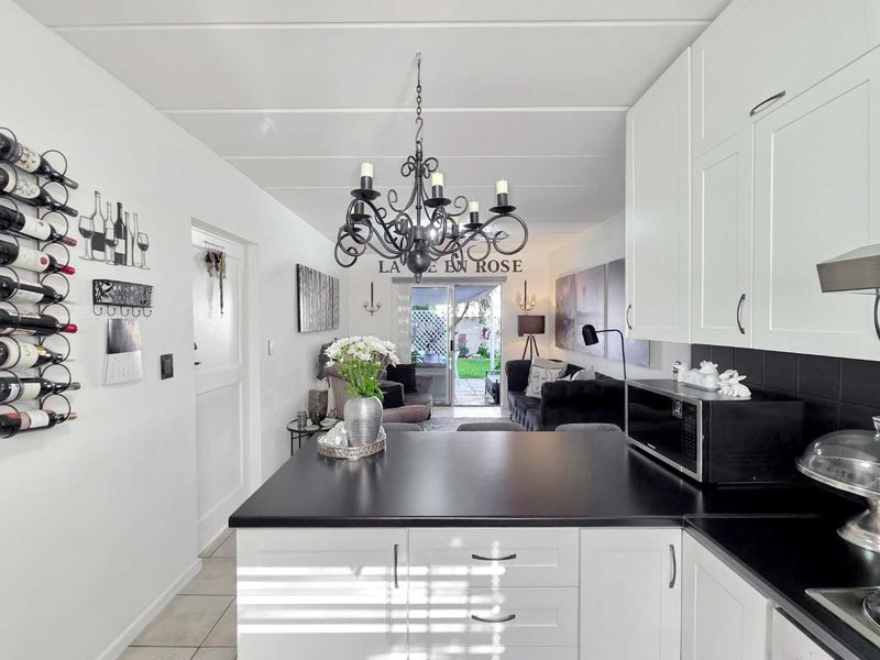 An open-plan kitchen and living area featuring white cabinetry, black countertops, and direct access to an outdoor patio through sliding glass doors.