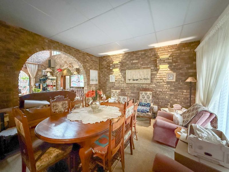 Dining room featuring exposed brick walls, a distinctive brick archway, and suspended ceiling tiles, offering a rustic aesthetic with potential for modernization.