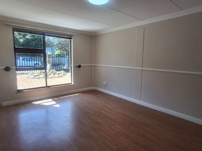 A bright, empty bedroom featuring laminate flooring, neutral wall tones, and a large sliding window with a view of the front exterior.