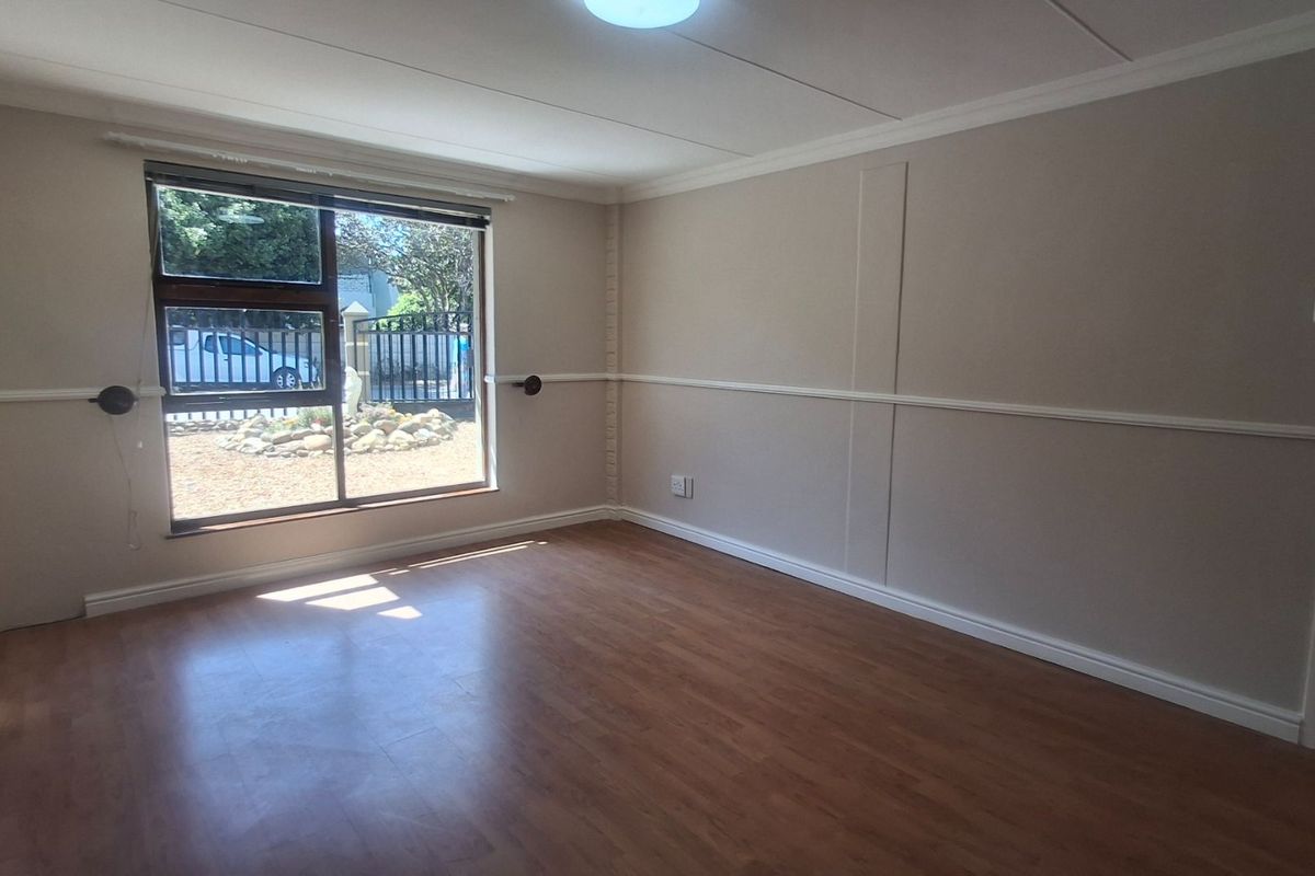 A bright, empty bedroom featuring laminate flooring, neutral wall tones, and a large sliding window with a view of the front exterior.