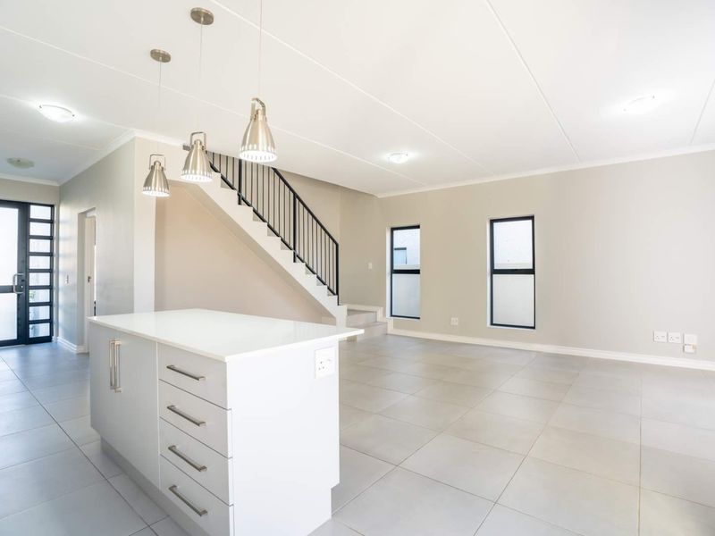 Spacious open-plan living area featuring a modern kitchen island, neutral tiled flooring, and a staircase with a sleek metal balustrade.