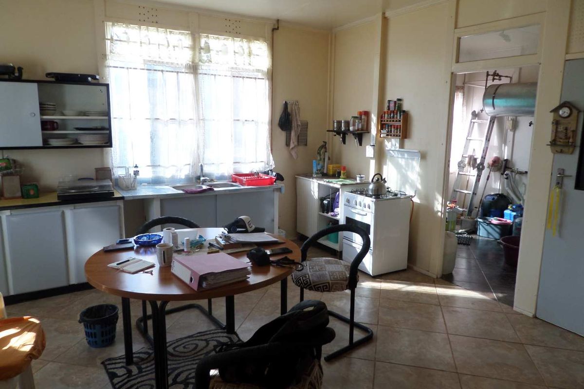 A dated kitchen featuring basic cabinetry, a freestanding stove, and tiled flooring, with an adjacent utility area visible through the doorway.
