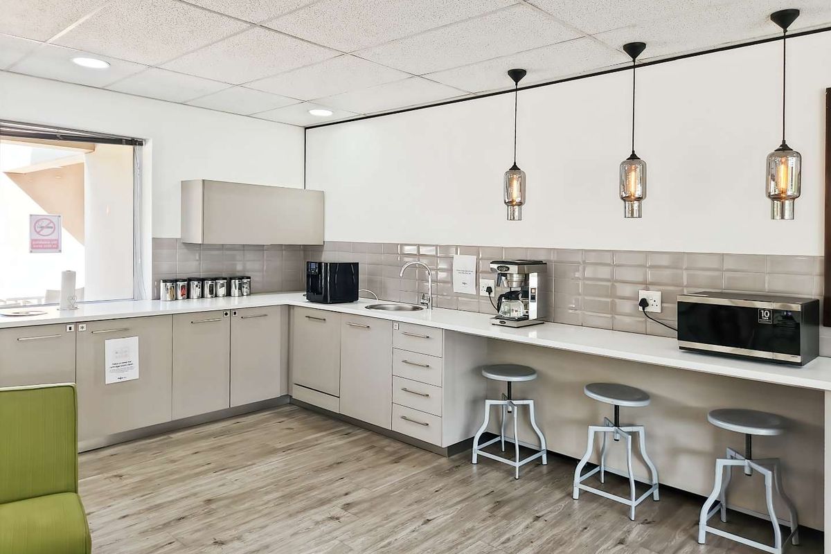 A modern office kitchenette featuring light grey cabinetry, a sleek countertop, subway tile backsplash, and contemporary pendant lighting.
