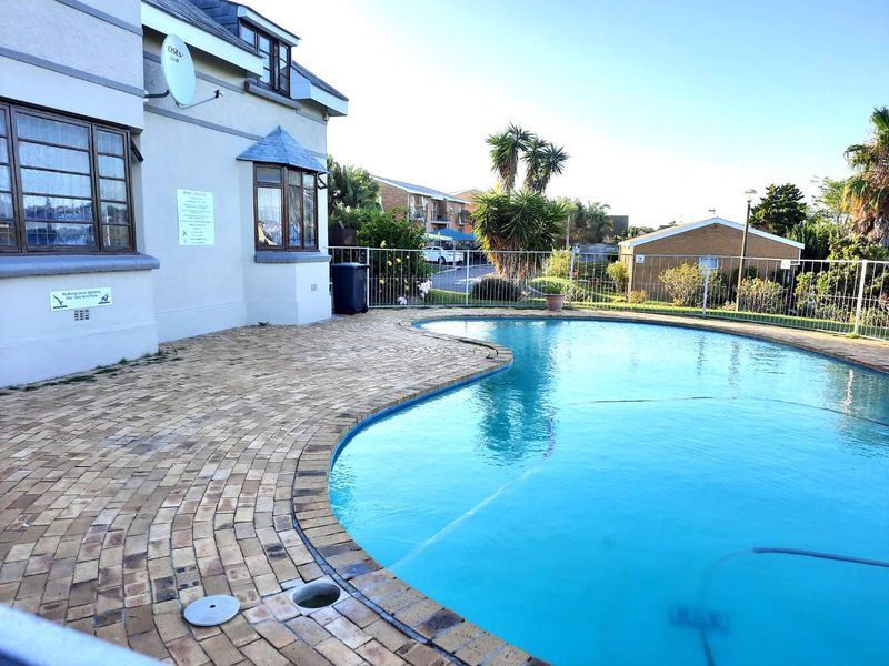 A well-maintained swimming pool area featuring brick paving surround and secure metal perimeter fencing, adjacent to the main building structure.