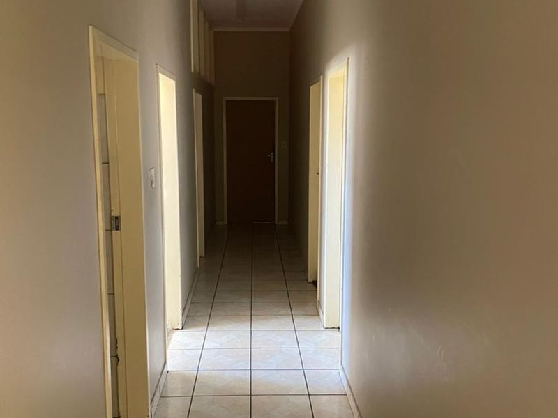 A long, empty residential hallway featuring tiled flooring and multiple doorways leading to various rooms, requiring cosmetic updates to the ceiling and finishes.