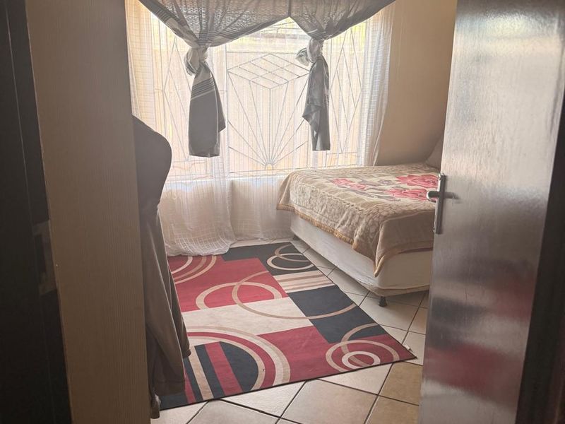 A bedroom featuring tiled flooring and a window with security bars, viewed from the doorway.