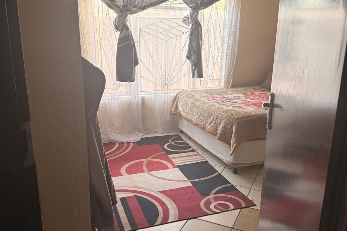 A bedroom featuring tiled flooring and a window with security bars, viewed from the doorway.