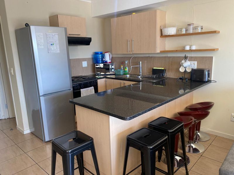 Compact kitchen featuring light wood cabinetry, granite countertops, a breakfast bar, and tiled flooring, providing a functional and efficient cooking space.
