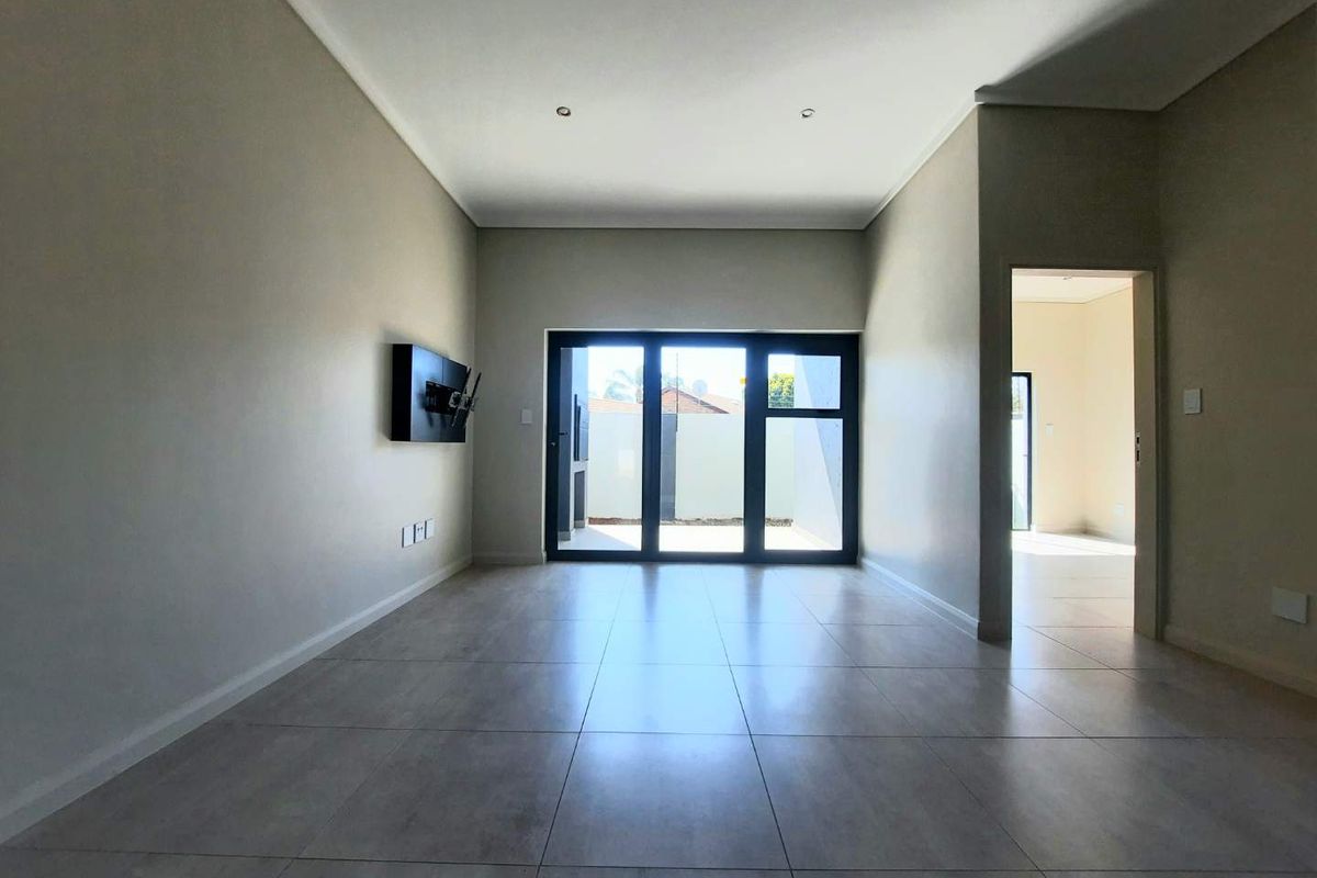 A bright, empty living room featuring neutral tiled flooring, recessed lighting, and large sliding glass doors leading to an outdoor area.