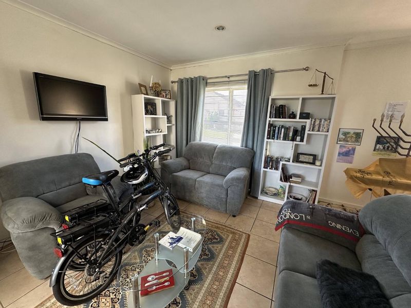 A comfortable living room featuring tiled flooring, recessed lighting, and large windows with venetian blinds, offering a functional space for relaxation.