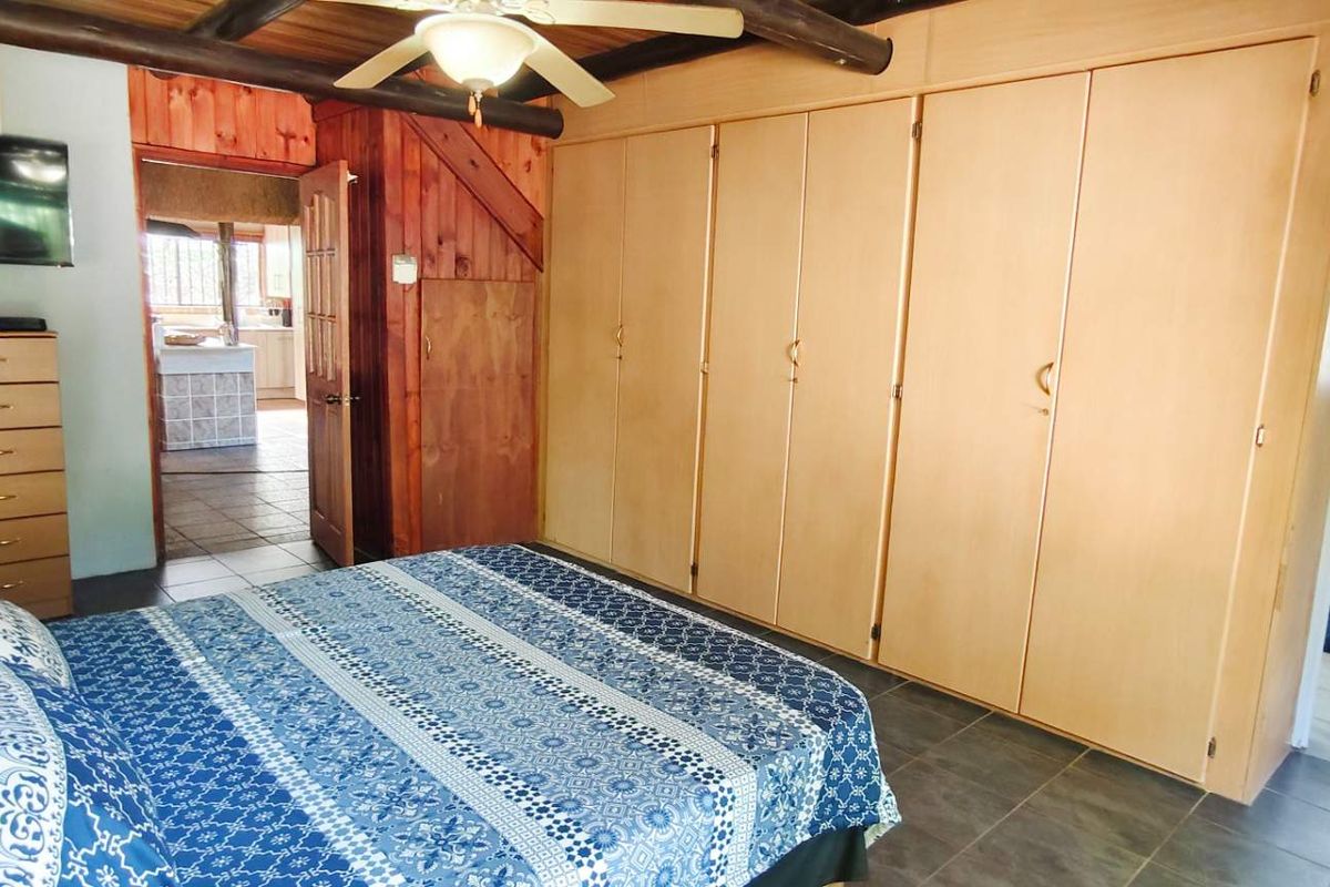Bedroom featuring built-in wooden cupboards, exposed timber ceiling beams, and an en-suite bathroom with tiled flooring.
