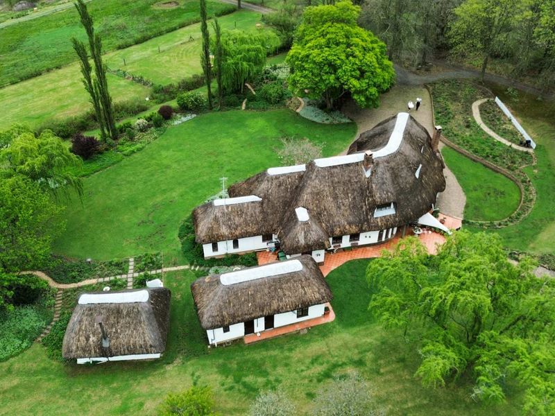 Aerial view of a property featuring multiple buildings with traditional thatched roofs, surrounded by extensive landscaped gardens and mature trees.