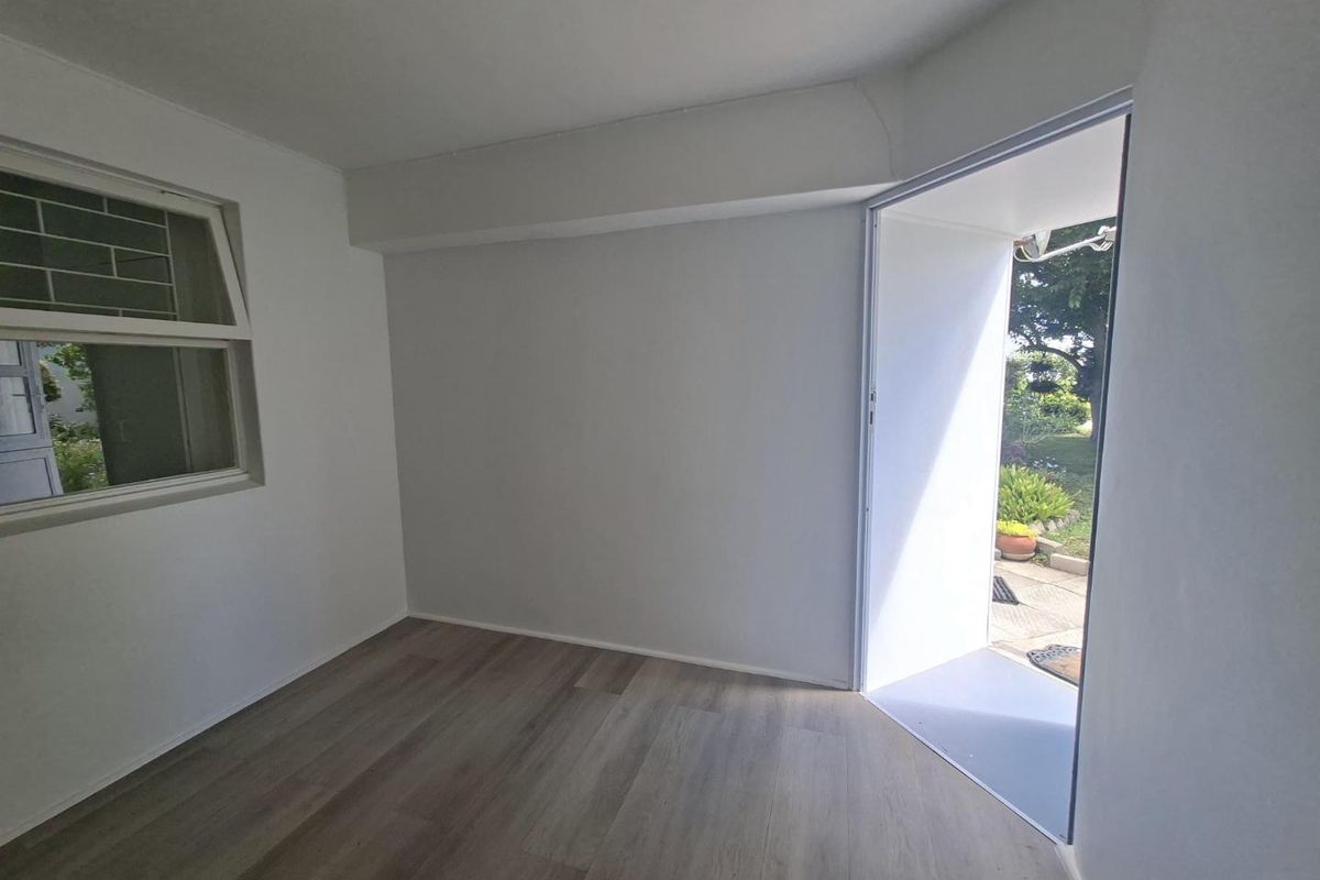 A bright, empty living area featuring modern laminate flooring and direct access to an outdoor garden space.