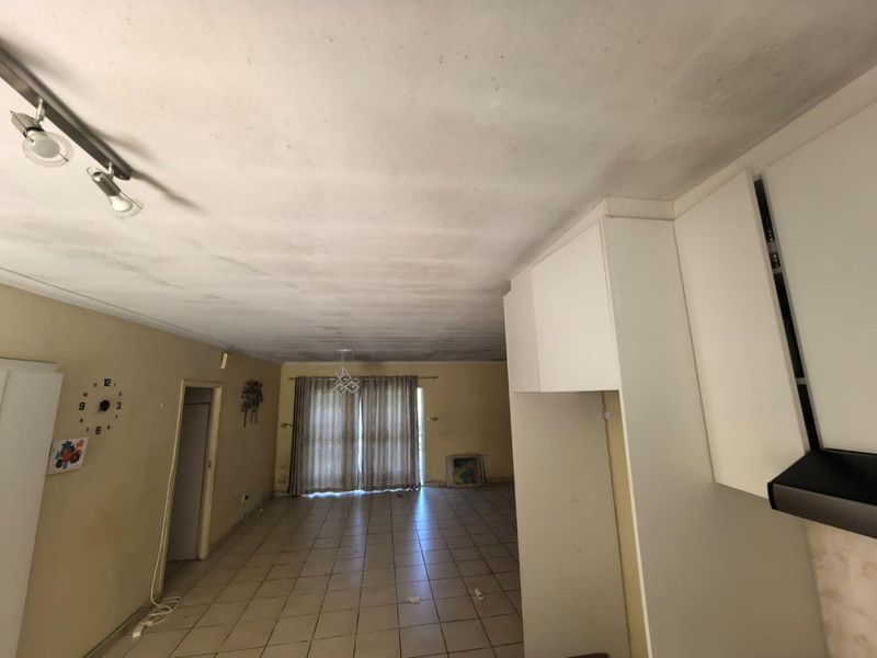 Open-plan living and kitchen area featuring tiled flooring, built-in cabinetry, and sliding door access to the exterior, requiring cosmetic updates to the ceiling and walls.