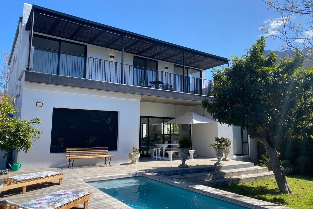 Rear view of a modern two-story house featuring a swimming pool, wooden decking, and a spacious covered balcony.