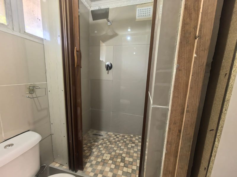 A bathroom featuring a tiled shower enclosure with a modern shower head, toilet, and wall tiling, currently requiring finishing touches to the door frame.
