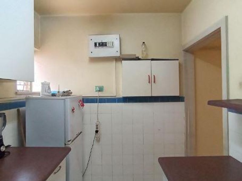 A dated kitchen area featuring built-in cabinetry, tiled splashbacks, and an exposed electrical distribution board, offering potential for modernization and renovation.