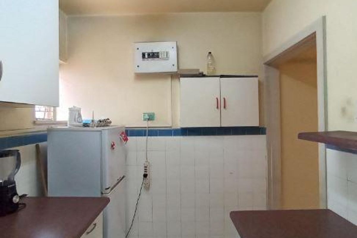 A dated kitchen area featuring built-in cabinetry, tiled splashbacks, and an exposed electrical distribution board, offering potential for modernization and renovation.