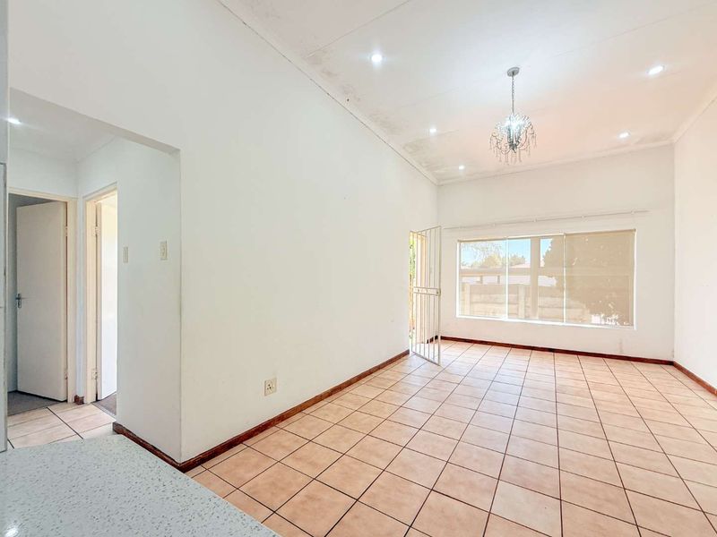 An empty living room featuring tiled flooring, recessed lighting, a decorative chandelier, and a security gate leading to the exterior.