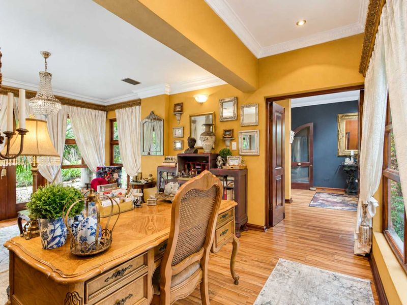A well-maintained home office featuring warm yellow walls, hardwood flooring, crown molding, and an open archway leading to an adjacent hallway.