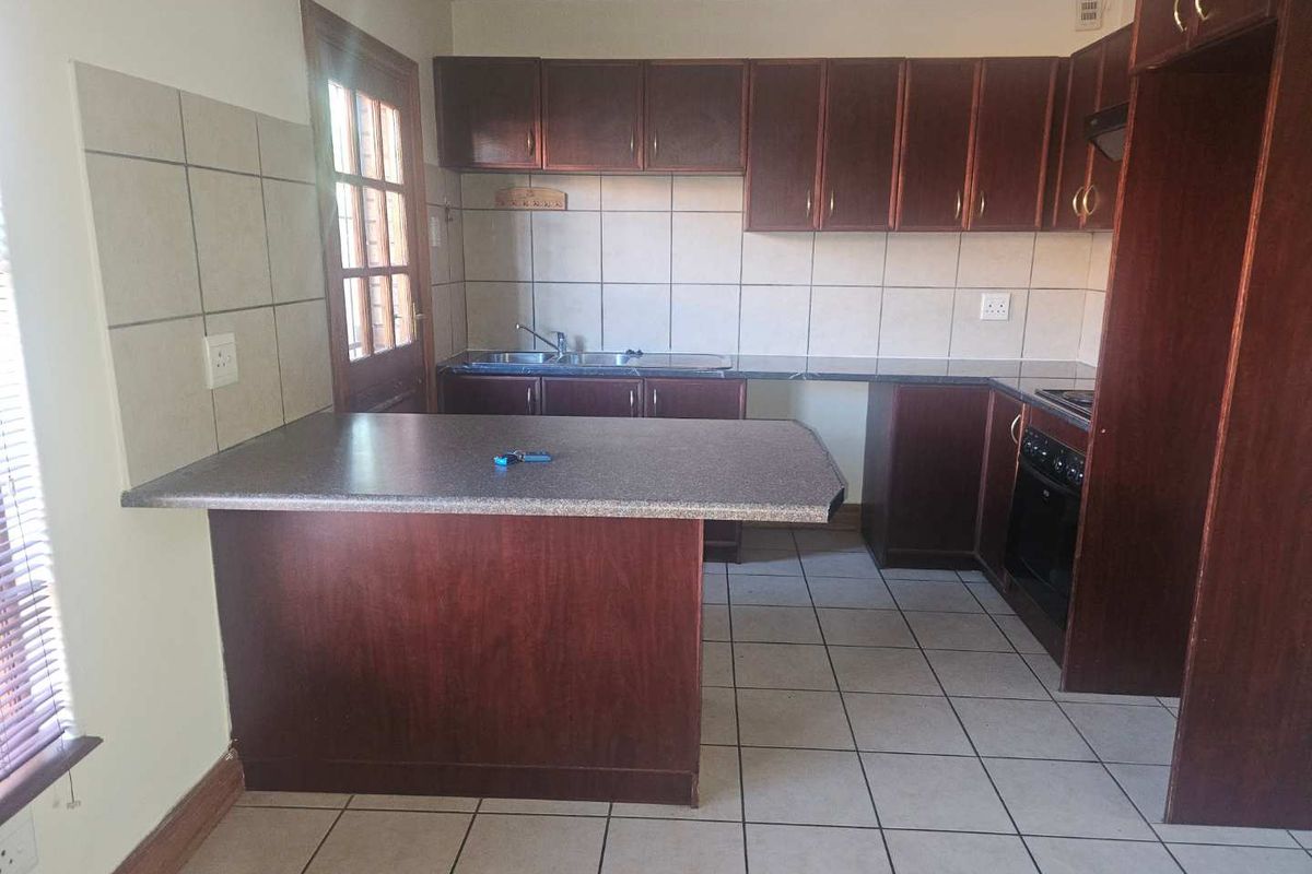 A functional kitchen featuring dark wood cabinetry, laminate countertops, a built-in oven and hob, and tiled flooring with direct access to the exterior.