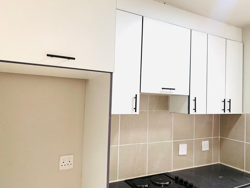 A clean, modern kitchen featuring white cabinetry, a tiled backsplash, and a built-in electric hob with dark laminate countertops.