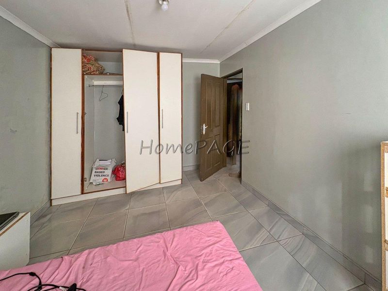 A bedroom featuring tiled flooring, a built-in wardrobe, and a coved ceiling. The room requires cosmetic attention to the ceiling finish.