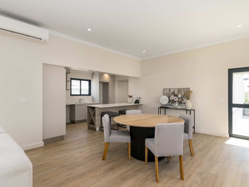 Modern open-plan living and dining area featuring light laminate flooring, recessed lighting, a split-system air conditioner, and a functional kitchen with a breakfast island.