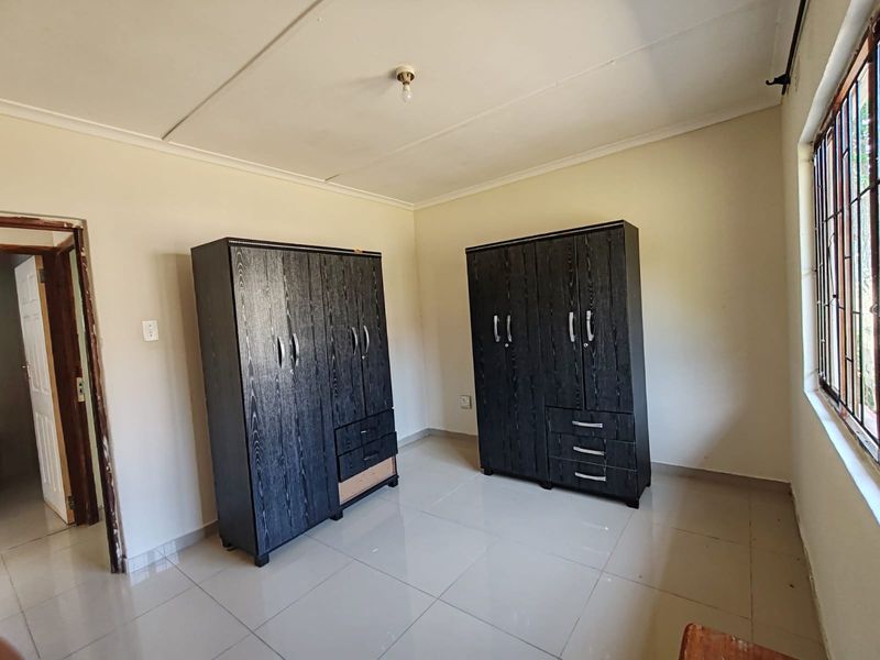 A bedroom featuring tiled flooring and security bars on the window, with visible ceiling panel damage requiring maintenance.