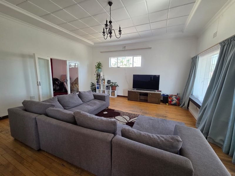 Spacious living room featuring original hardwood flooring, a decorative coffered ceiling, and classic french doors leading to an adjacent room.